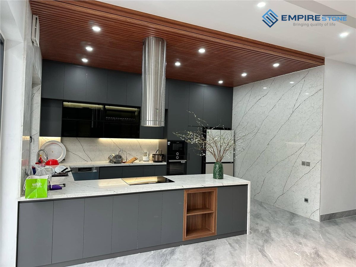 Bếp chữ U tủ xám, mặt đá và mảng tường ốp đá trắng vân xám chạy từ sàn đến trần