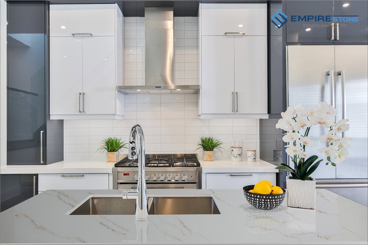 Đá ốp bếp phong cách Bắc Âu: Chọn màu, vân và cách phối với gỗ sáng Bếp trắng tối giản mặt đá vân xám nhẹ, chậu rửa inox và bình hoa lan trắng